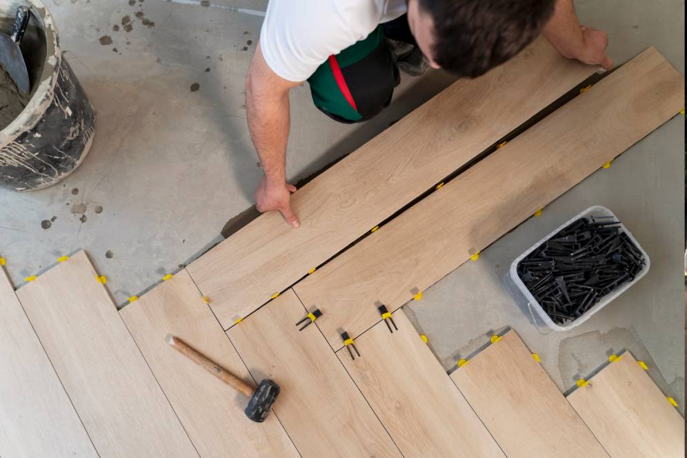 Person installing wooden floor tiles with tools and spacers visible.