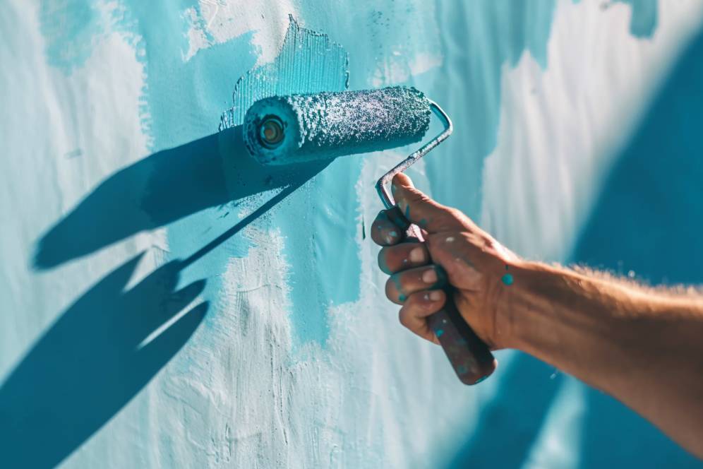 A hand holding a paint roller applying blue paint to a wall